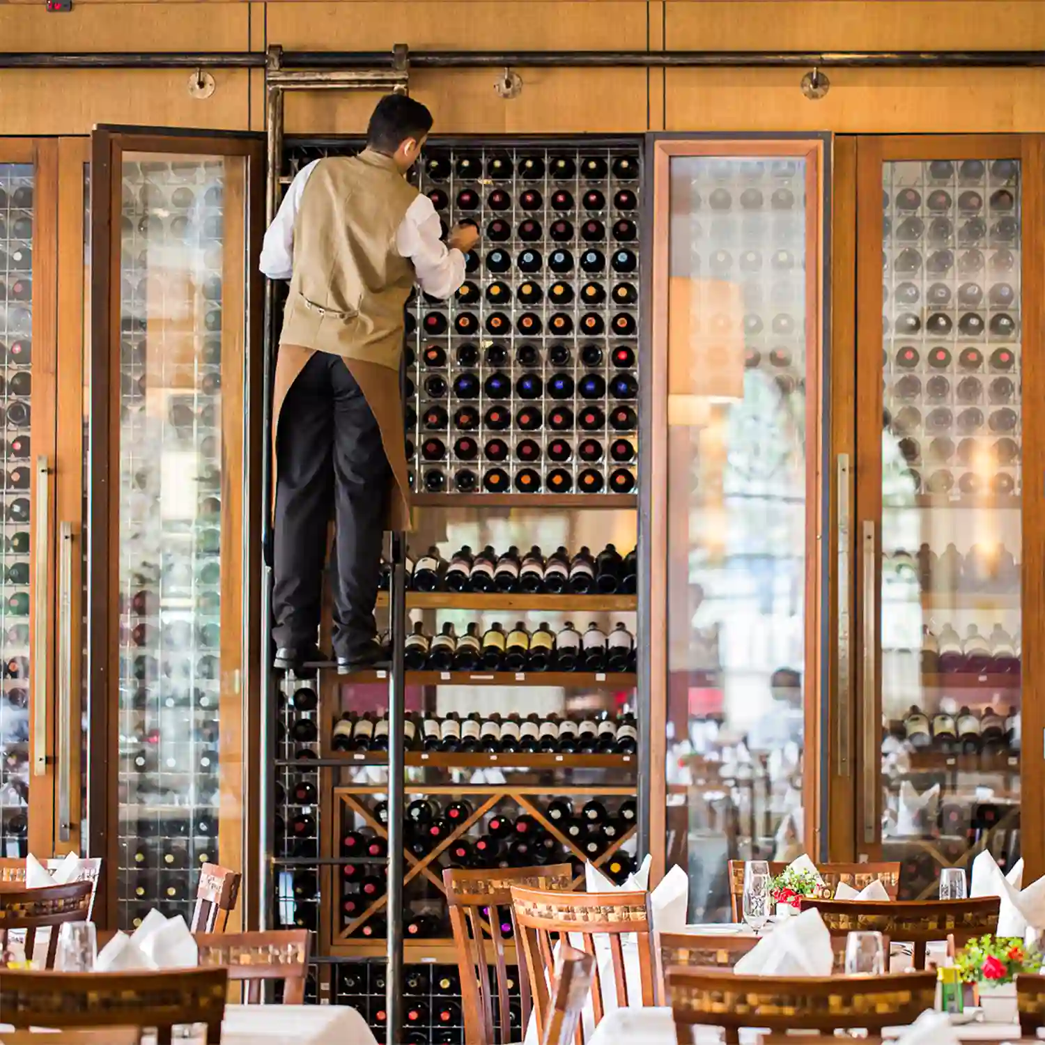 Foto do salão da Jadineira: funcionário organizando garrafas na adega envidraçada do restaurante